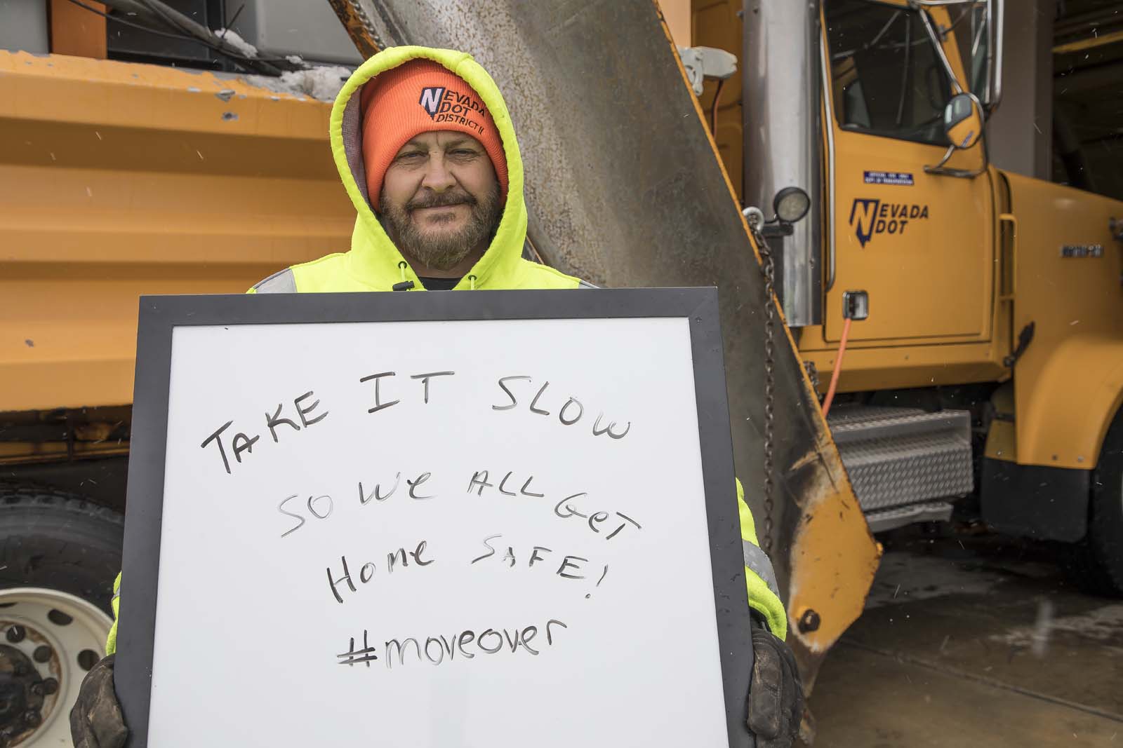 An NDOT employee holding a sign for drivers to go slowly in winter conditions